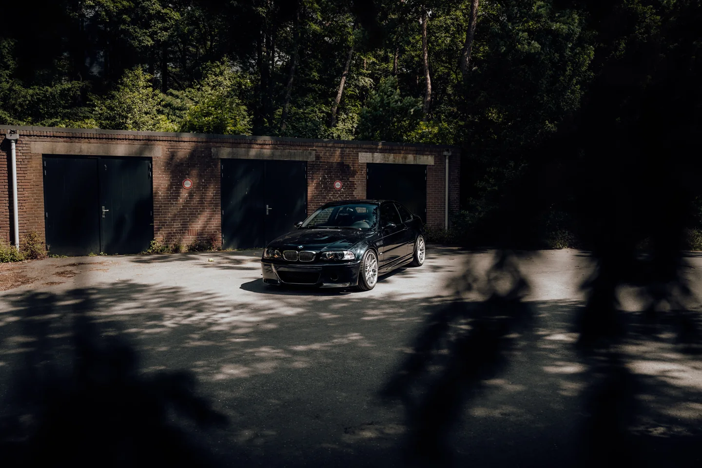 Dark BMW in front of garages in hard sunlight