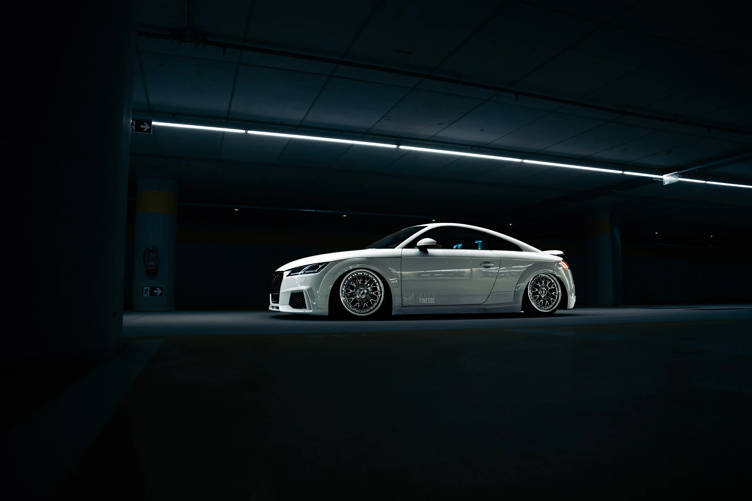 White Audi TT beneath strip lighting in a dark parking garage